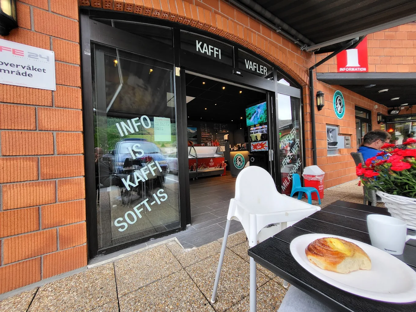 Forsiden av Stabukk Olden. På bordet er det et stort brød med en gul vaniljekjerne. Glassdørene til kafeen har store hvite bokstaver som reklamerer for kaffe, iskrem, informasjon og brus.