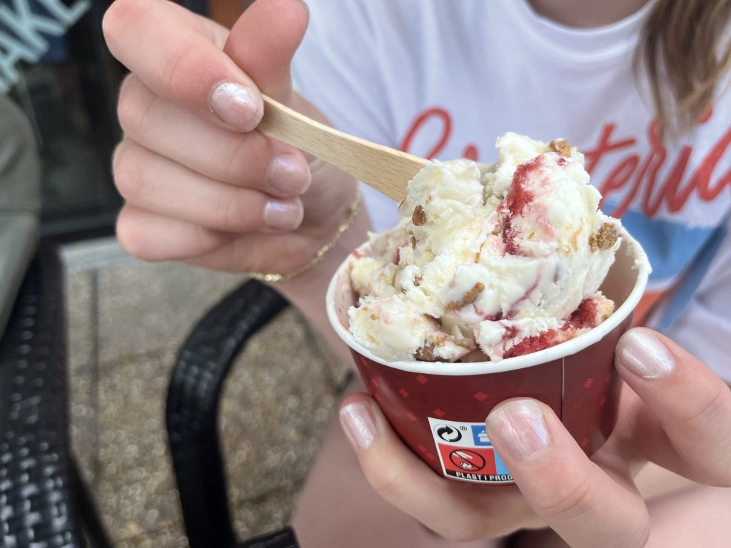Jente som holder en ostekake-is i en rød kopp fra Stabukk kafé. Hun øser den opp med en tresleiv.