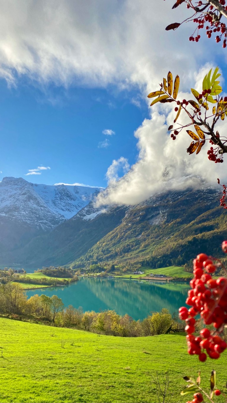 Kvinne padler kajakk på en speilblank fjordsjø i Olden, Norge, med snødekte fjell speilet i det turkise vannet på en solrik sommerdag