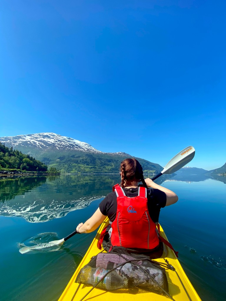 Sykkelgruppe passerer Olden kirke på en guidet sykkeltur i Olden, Norge, med dramatiske snødekte fjell i bakgrunnen