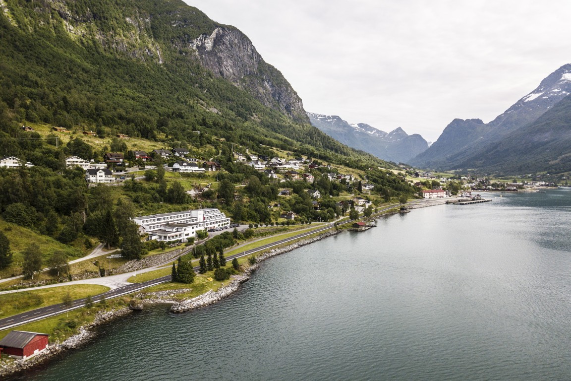 Et luftfoto av bygda, som viser de klare fjordene og de høye fjellsidene. Blant det grønne gresset til venstre kan man se det store hvite Olden Fjordhotel.