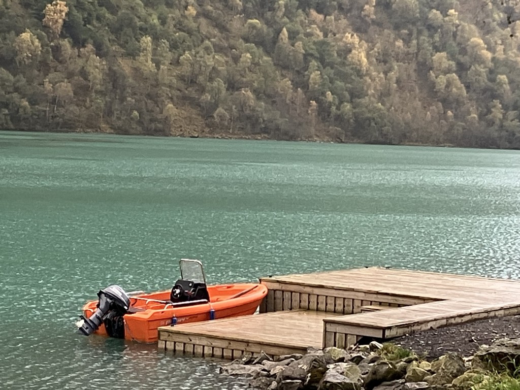 En oransje båt som flyter i den grønne fjorden ved Flåten i Olden. Vannet er stille uten bølger.