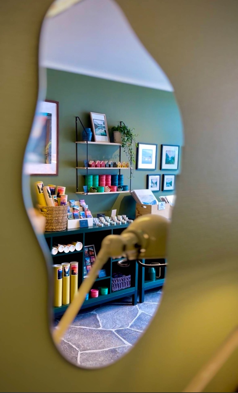 Interiør i Olden-gavebutikken speilet i dekorativt speil, som viser hyller med norske suvenirer, fargerike bokser, innrammede fjordtrykk og lokale produkter