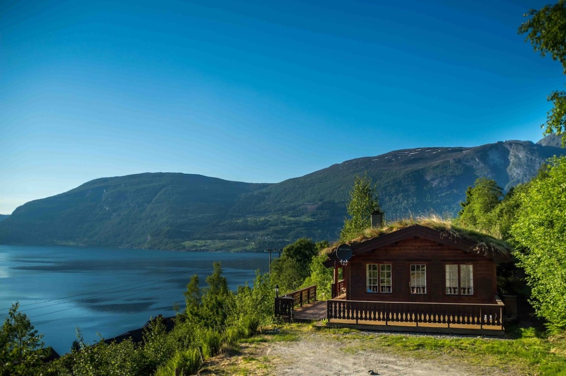 Tradisjonell norsk tømmerhytte med gresstak med utsikt over Oldevatnet og fjellfjordlandskapet i Olden, Norge