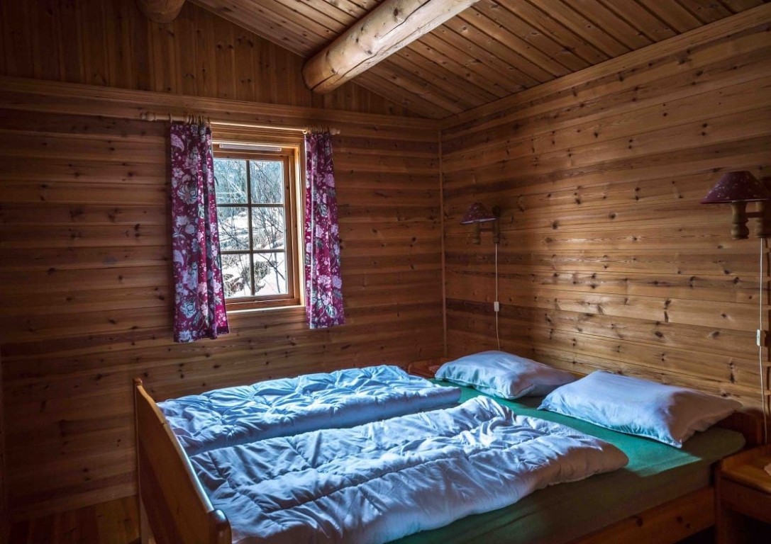 Dobbelt soverom i en norsk tømmerhytteutleie i Olden, med furuwegger, blomstrete gardiner og en snøhvit vinterutsikt