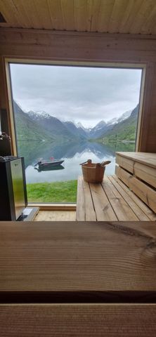 Innvendig utsikt fra Olden Camping-saunaen med utsikt over Oldevatnet og snødekte fjell gjennom et stort panoramavindu
