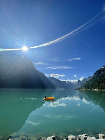 Person padler på det strålende turkise Oldevatnet på en solrik sommerdag i Olden, Norge, med fjell som speiler seg i vannet