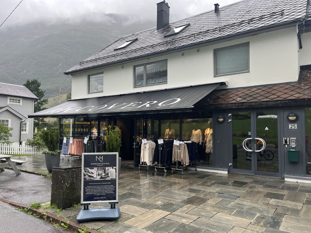 Riccovero motebutikks eksteriør i Olden, Norge, med utstilling av norsk kulturarvklær utenfor og fjellandskap i bakgrunnen