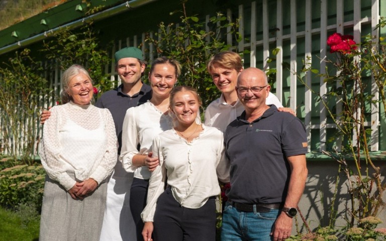 Familien og personalet på Singer gjestehus poserer i hagen i Olden, Norge – ønsker verter velkommen på et historisk norsk bed and breakfast