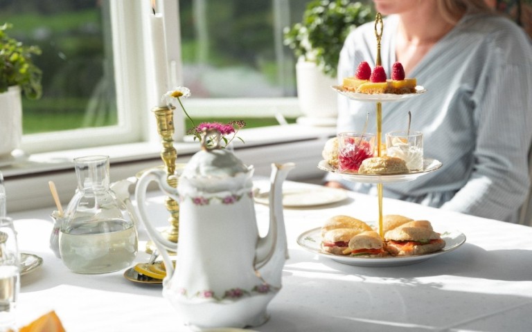 Tradisjonell afternoon tea med etasjevis kakefat, scones, smørbrød og antikk tekanne i porselen servert på Singer gjestehus i Olden, Norge
